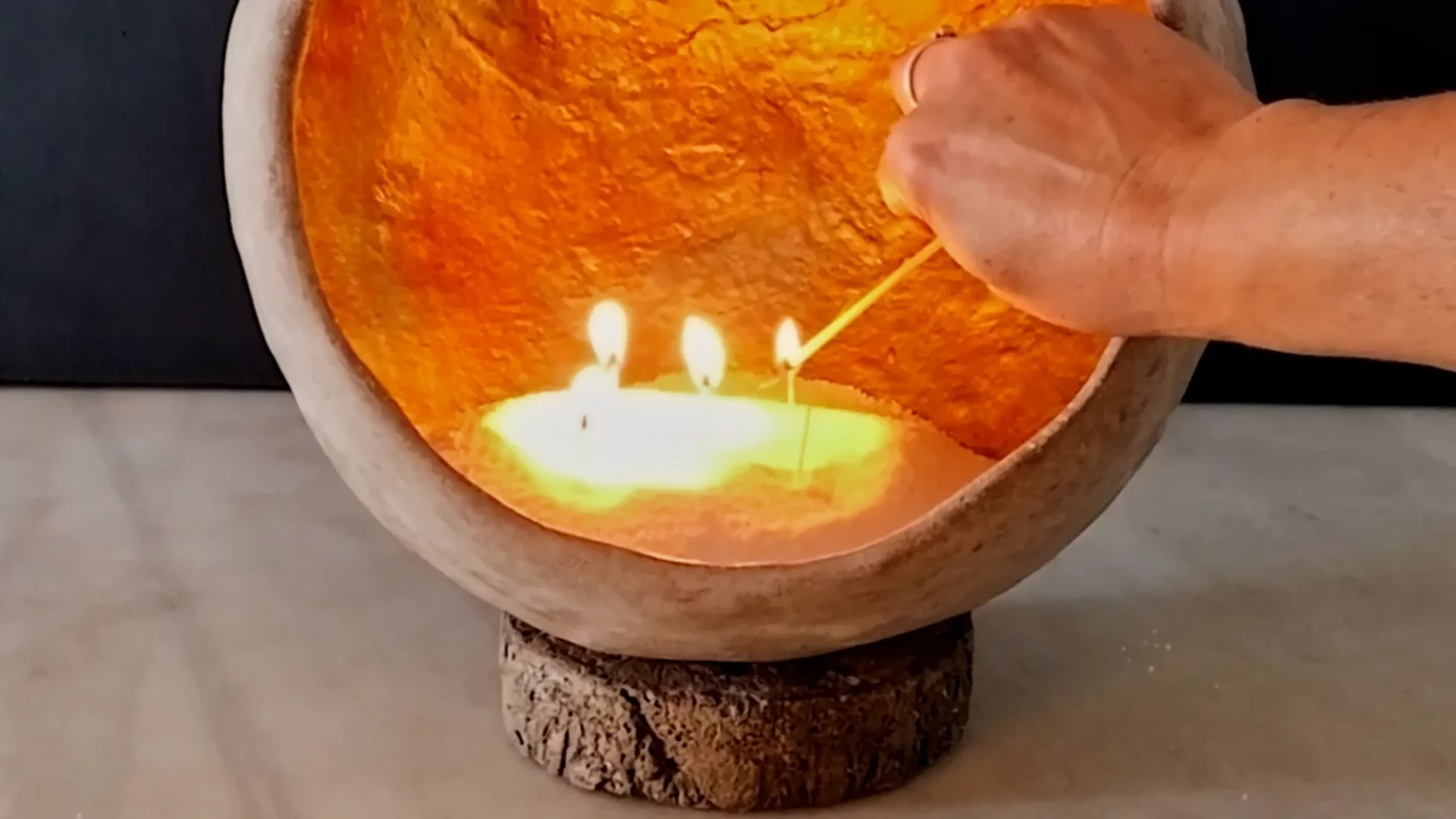 Mano activando el fuego central con cera de arena en una pieza de arte funcional en cemento crudo de 53 Design Lab durante una sesión de yoga.