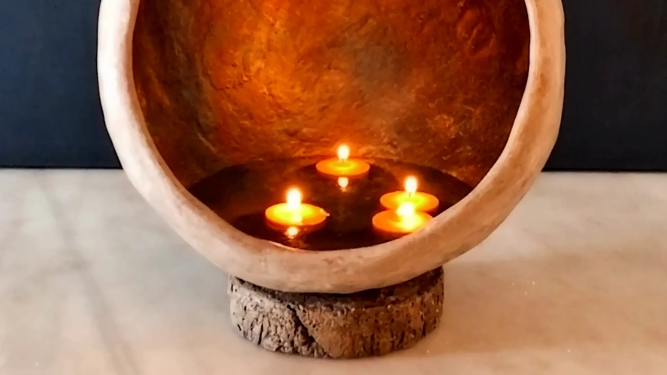 Velas flotantes encendidas sobre agua en el interior texturizado de una pieza de arte funcional en cemento crudo de 53 Design Lab, activando un ritual de aroma y relajación en un espacio wellness.